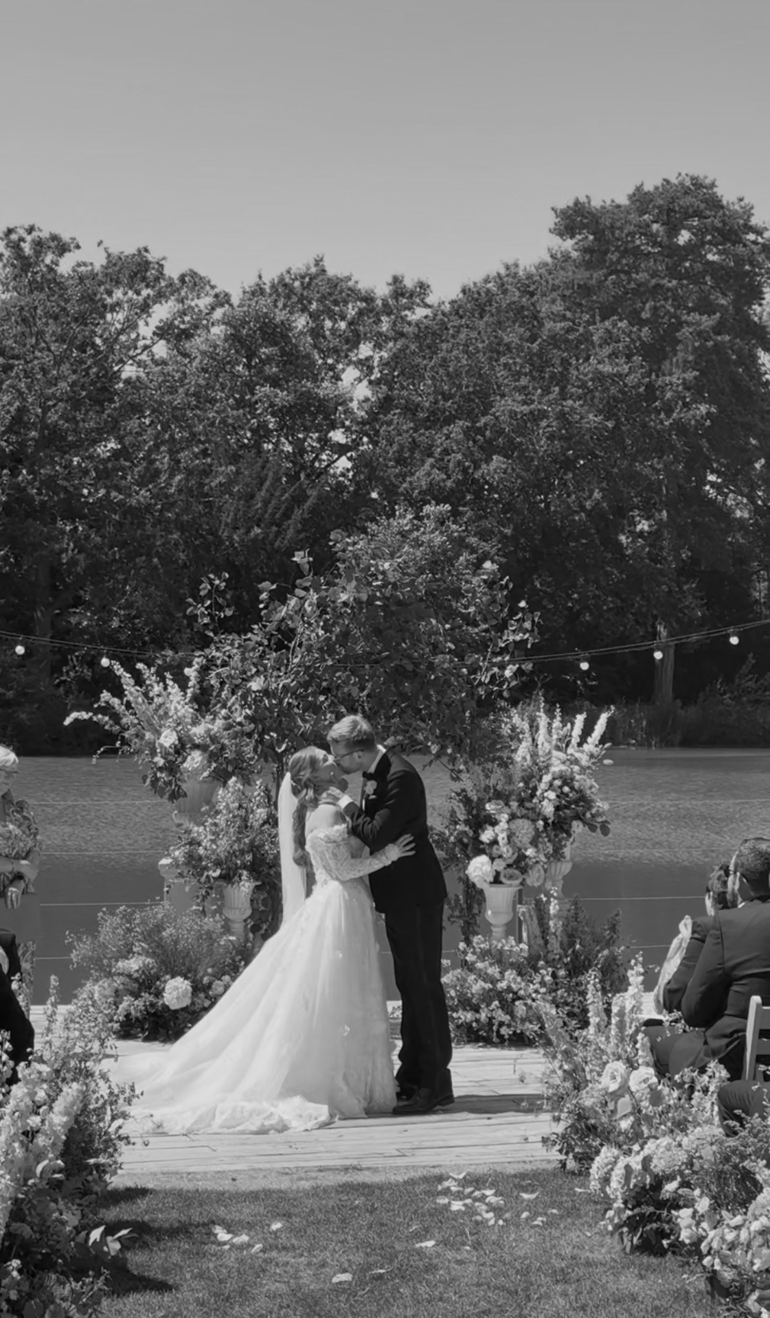 Outdoor ceremony kiss under a floral arch by the water